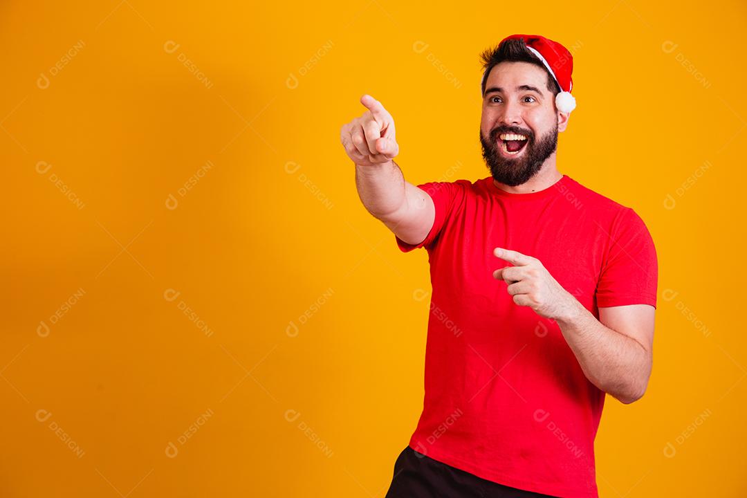 homem bonito vestido para o natal com chapéu de papai noel apontando promoção de fim de ano