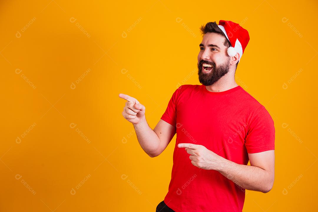 homem bonito vestido para o natal com chapéu de papai noel apontando promoção de fim de ano