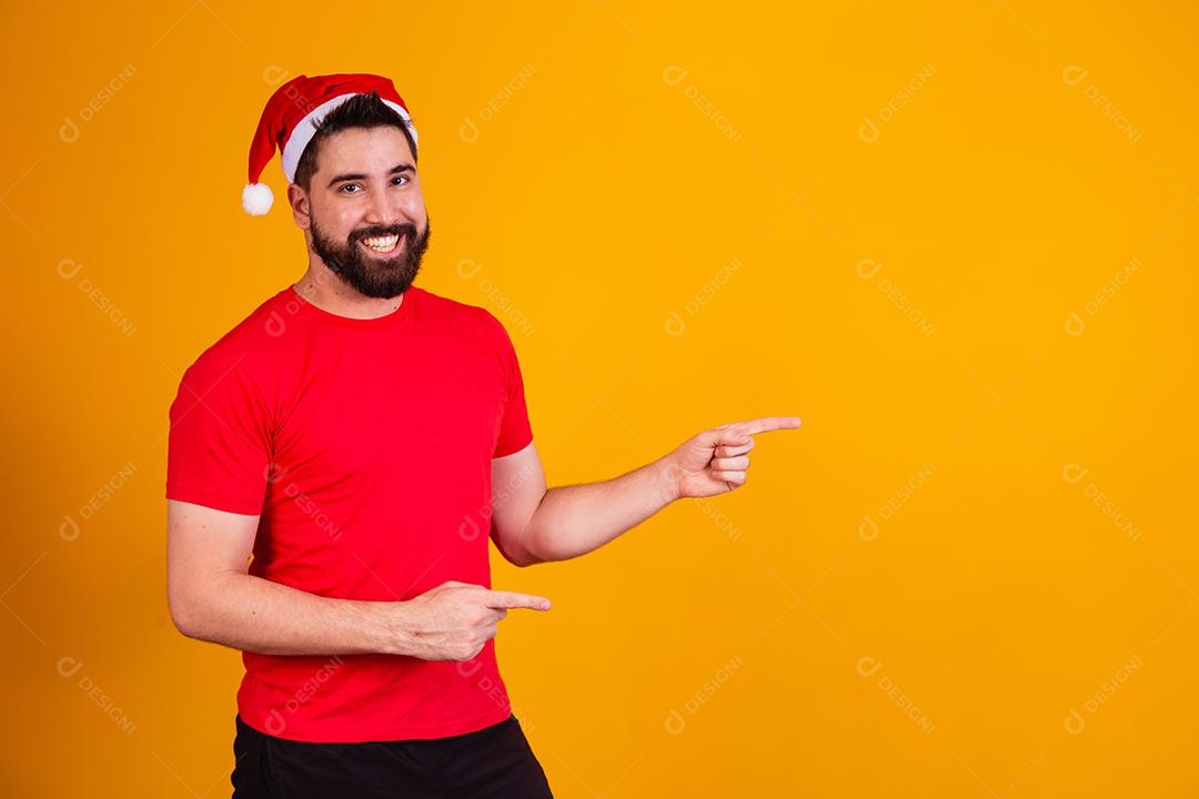 homem bonito vestido para o natal com chapéu de papai noel apontando promoção de fim de ano