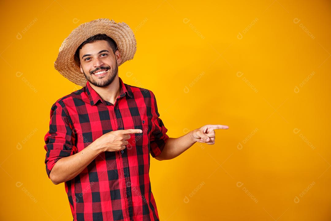 Homem brasileiro vestindo roupas típicas para a Festa Junina apontando para o lado