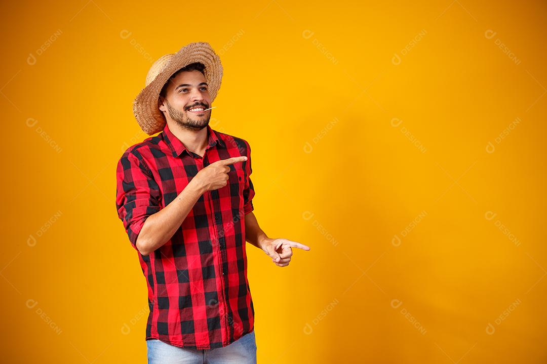 Homem brasileiro vestindo roupas típicas para a Festa Junina apontando para o lado