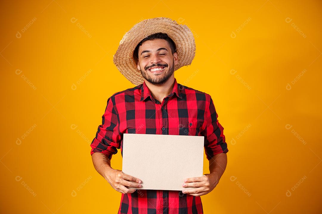 Homem brasileiro vestindo roupas típicas para a Festa Junina segurando placa