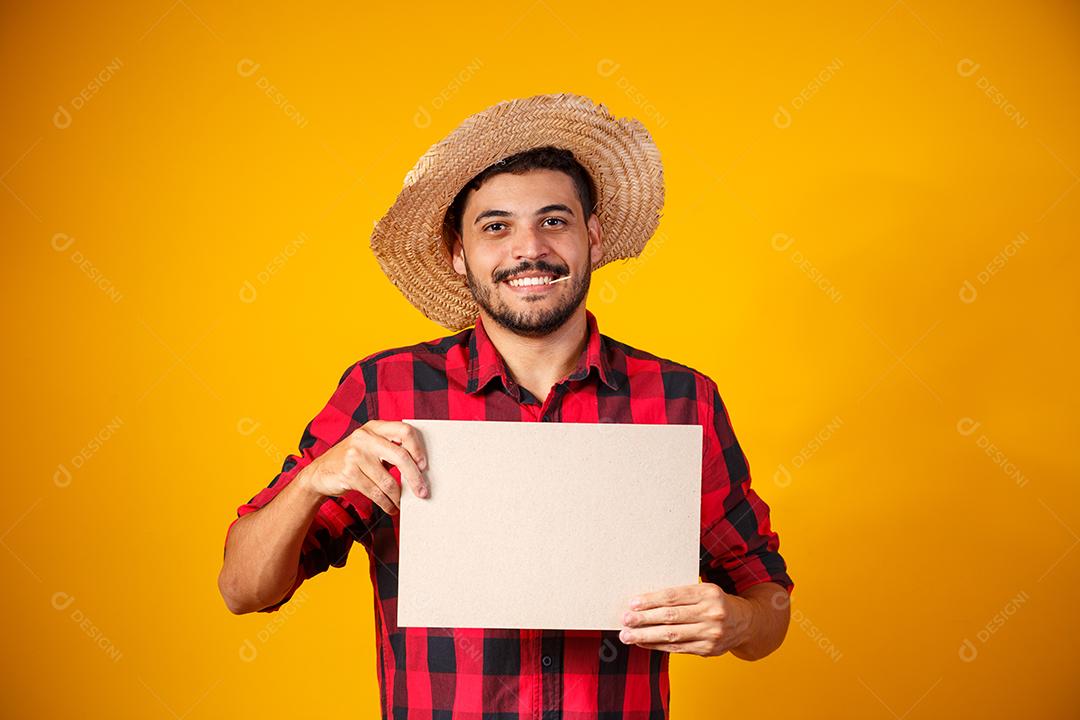 Homem brasileiro vestindo roupas típicas para a Festa Junina segurando placa
