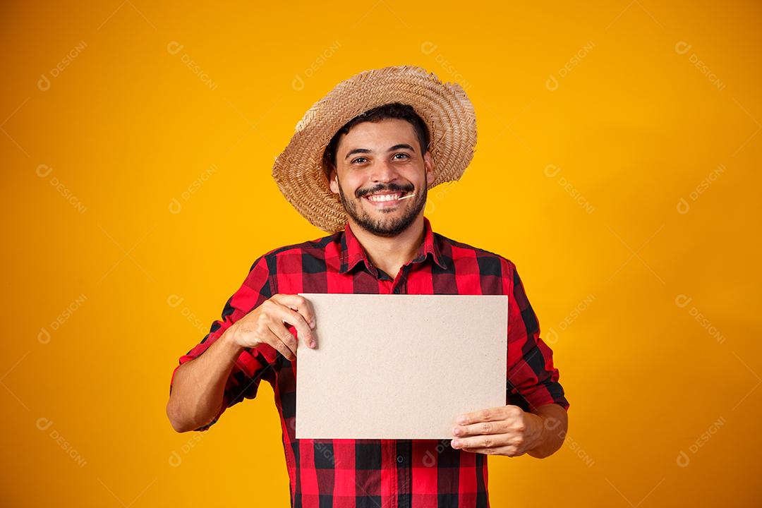 Homem brasileiro vestindo roupas típicas para a Festa Junina segurando placa