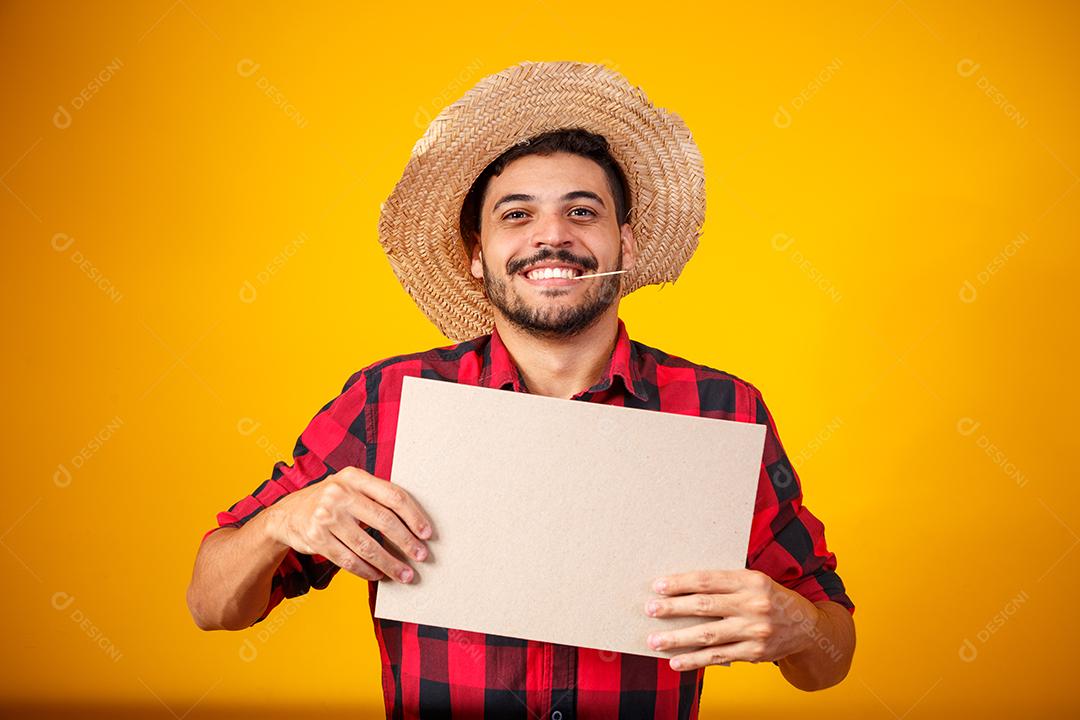 Homem brasileiro vestindo roupas típicas para a Festa Junina segurando placa