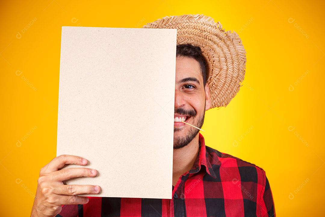 Homem brasileiro vestindo roupas típicas para a Festa Junina segurando placa com espaço para texto