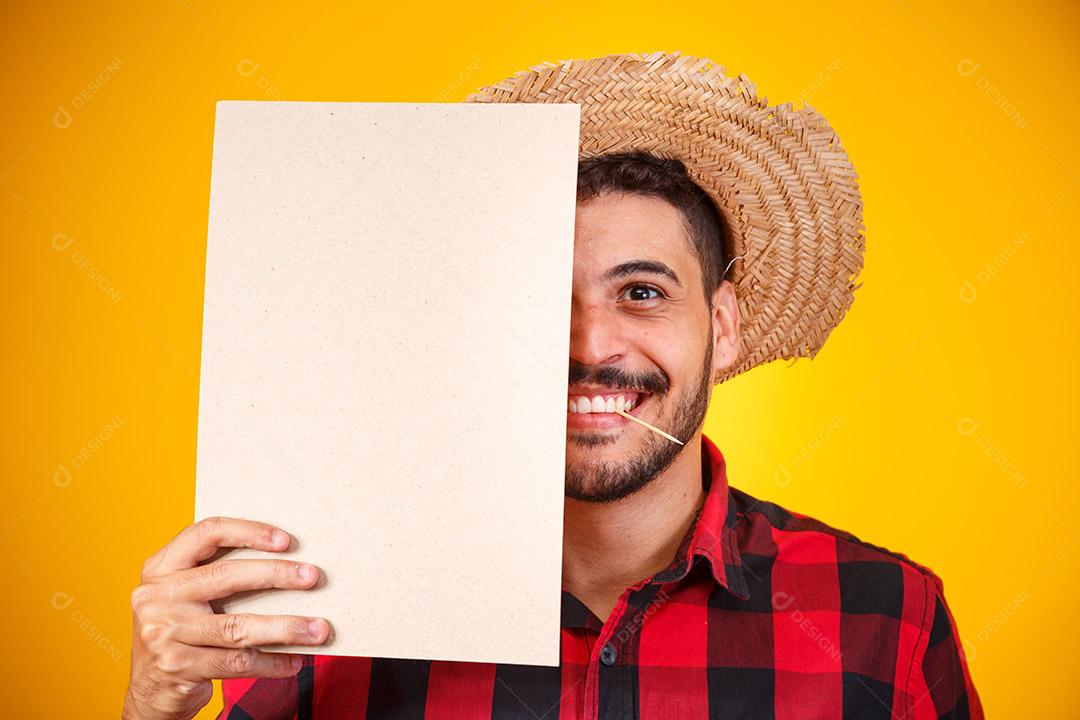 Homem brasileiro vestindo roupas típicas para a Festa Junina segurando placa com espaço para texto