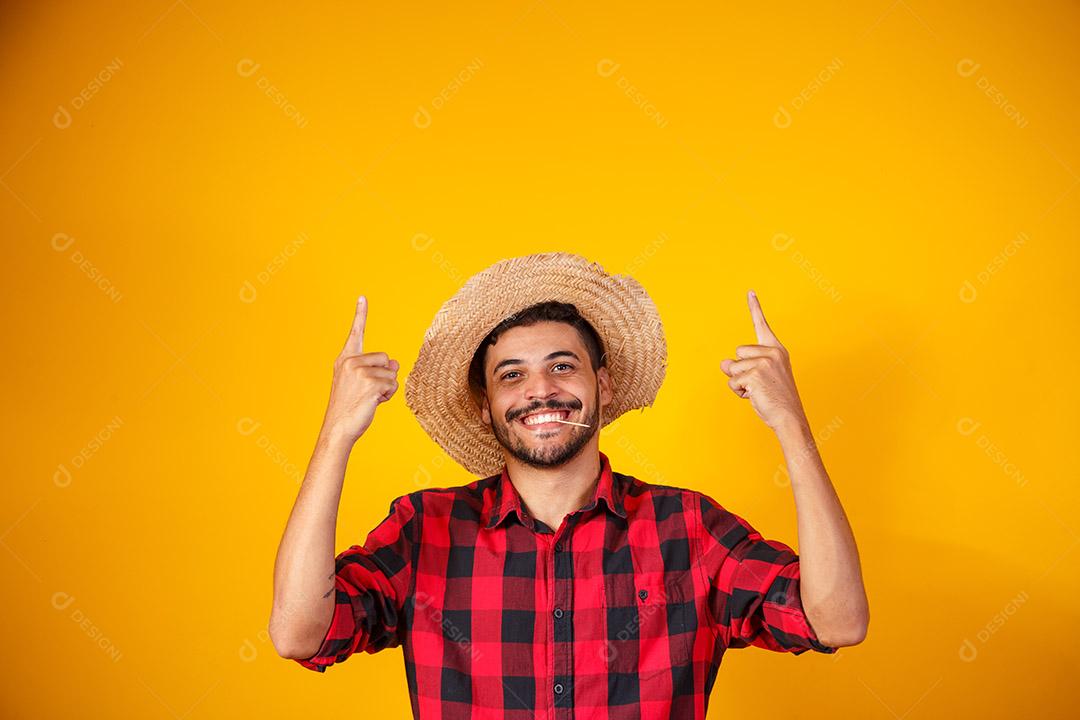 Homem brasileiro vestindo roupas típicas para a Festa Junina apontando para o lado com espaço para texto