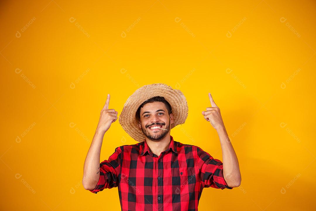 Homem brasileiro vestindo roupas típicas para a Festa Junina apontando para o lado com espaço para texto