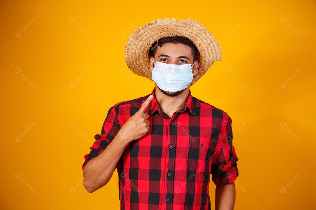 homem com roupas típicas da famosa festa brasileira chamada Festa Junina em comemoração ao São João. Menino lindo em fundo amarelo. Menino com traje de junho e máscara para prevenção do covid
