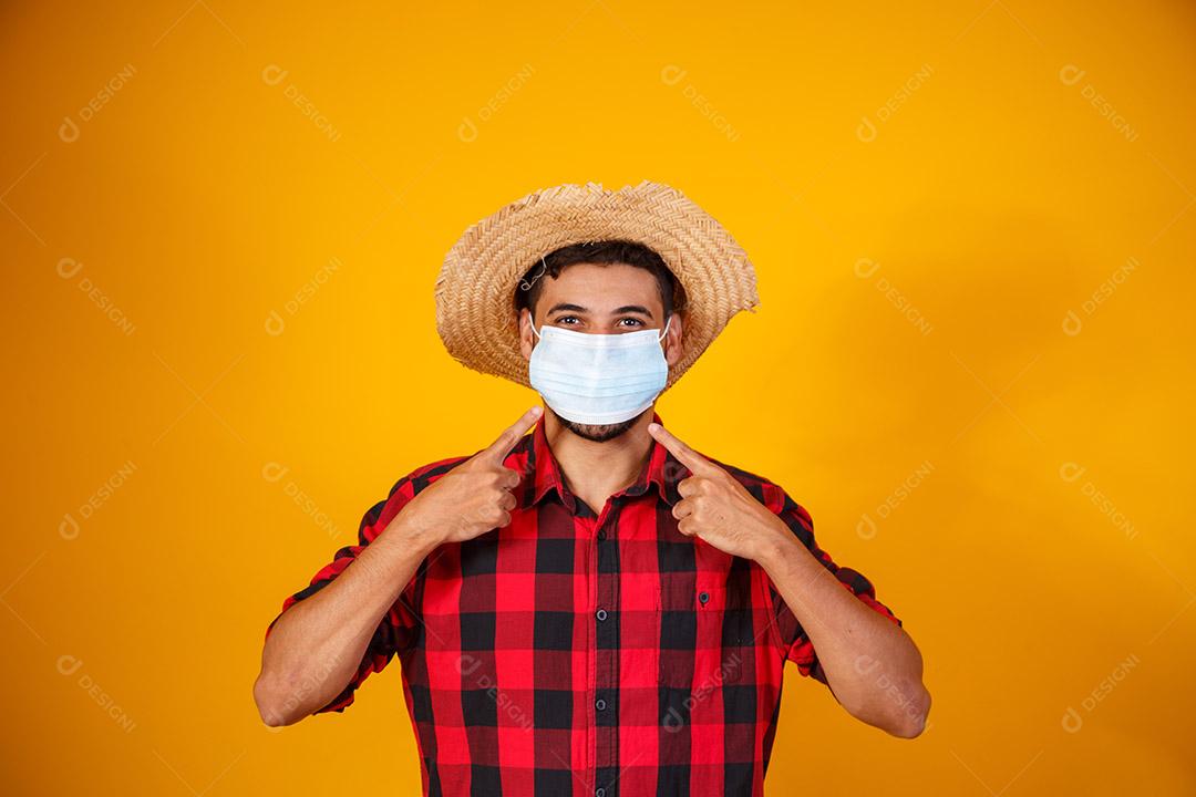 man with typical clothes of the famous Brazilian party called Festa Junina in celebration of São João. Beautiful baby boy on yellow background. Boy in June suit and mask for covid prevention