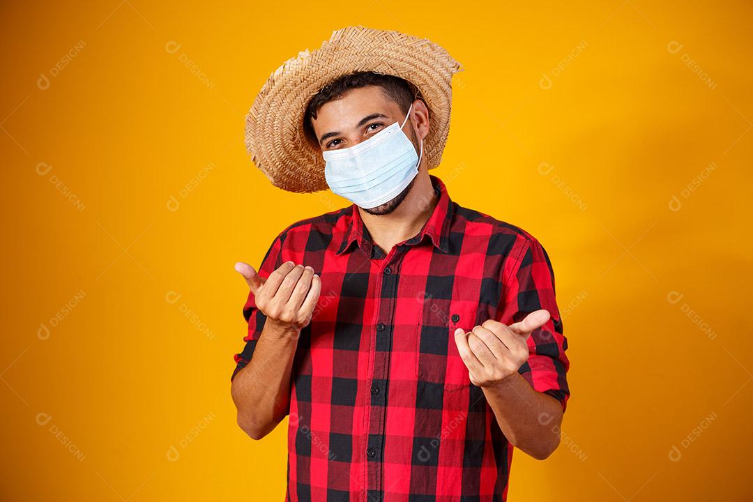 homem com roupas típicas da famosa festa brasileira chamada Festa Junina em comemoração ao São João. Menino lindo em fundo amarelo. Menino com traje de junho e máscara para prevenção do covid