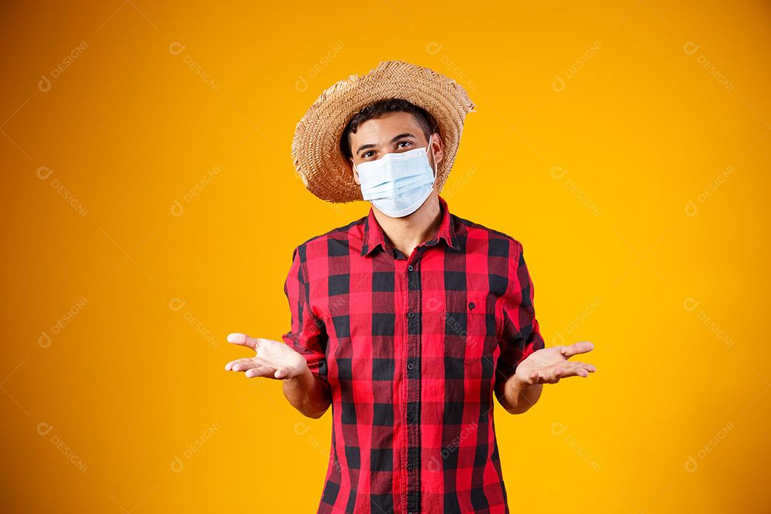 homem com roupas típicas da famosa festa brasileira chamada Festa Junina em comemoração ao São João. Menino lindo em fundo amarelo. Menino com fantasia de juno e máscara para prevenção de covid