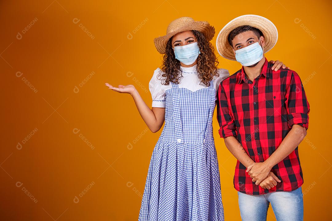 Casal vestindo roupas típicas para a Festa Junina e máscara de proteção para prevenção do COVID-19.