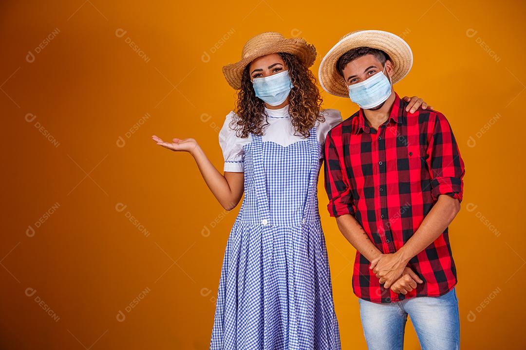 Casal vestindo roupas típicas para a Festa Junina e máscara de proteção para prevenção do COVID-19.