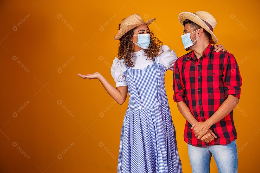 Casal vestindo roupas típicas para a Festa Junina e máscara de proteção para prevenção do COVID-19.