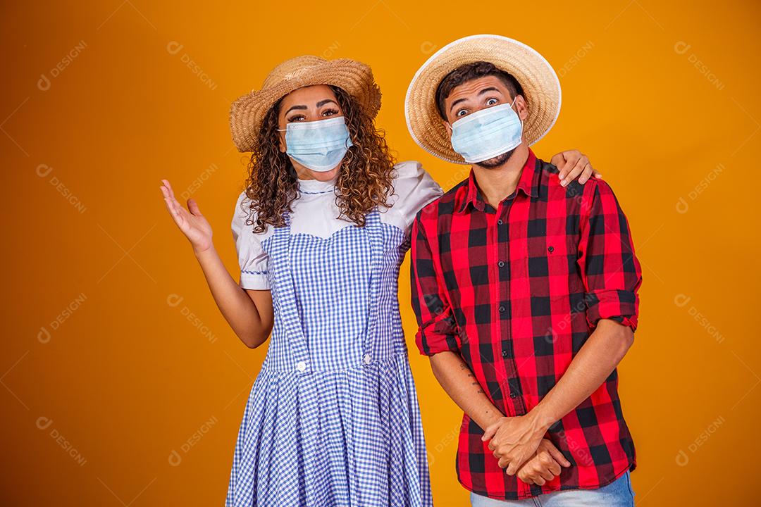 Casal vestindo roupas típicas para a Festa Junina e máscara de proteção para prevenção do COVID-19.