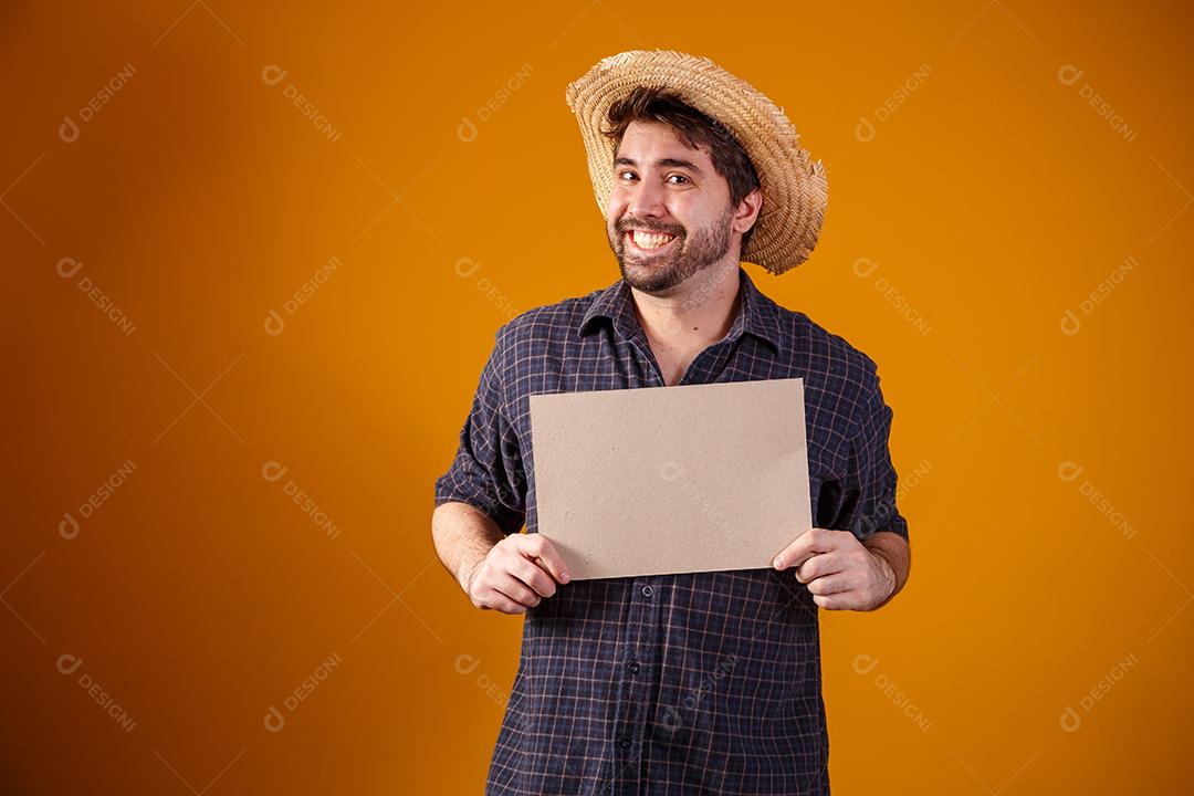 Homem usando chapéu de palha segurando placa sobre fundo amarelo