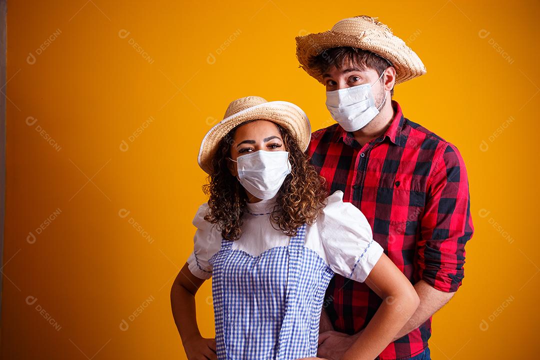 casal vestindo roupas típicas para a Festa Junina e máscara de proteção para prevenção do COVID-19.