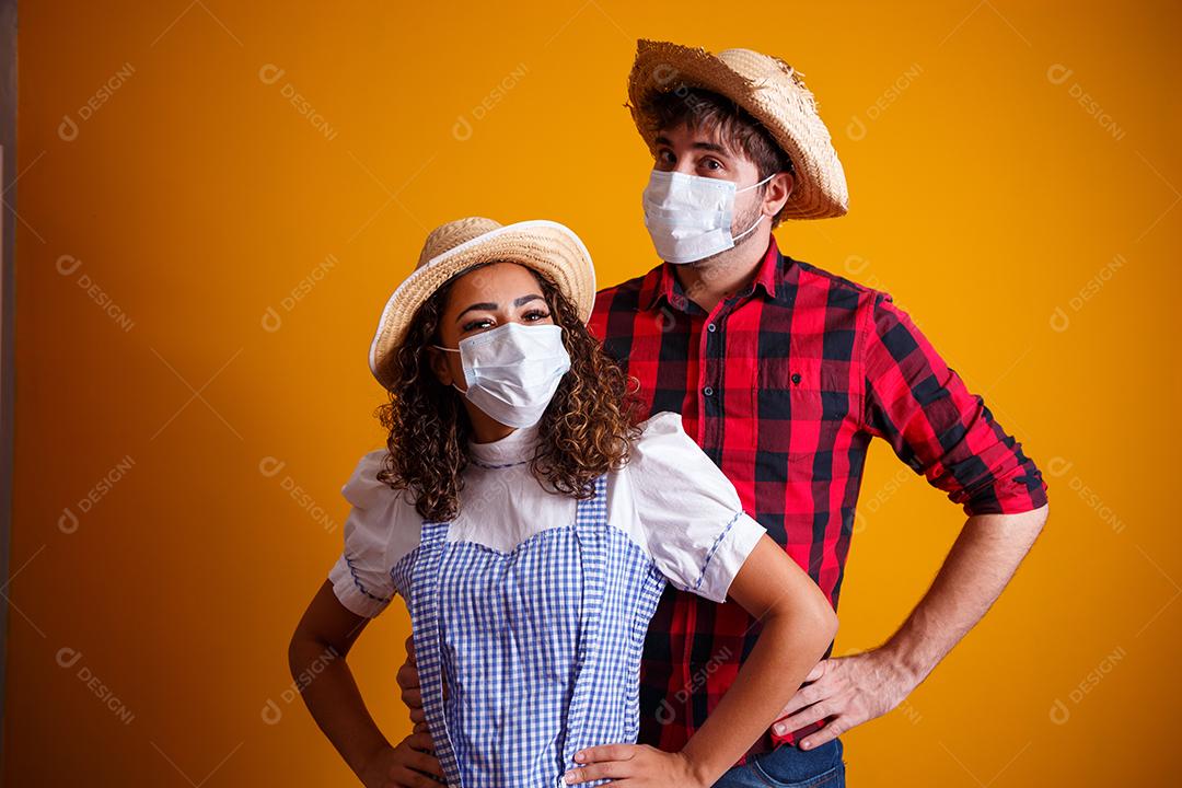 casal vestindo roupas típicas para a Festa Junina e máscara de proteção para prevenção do COVID-19.