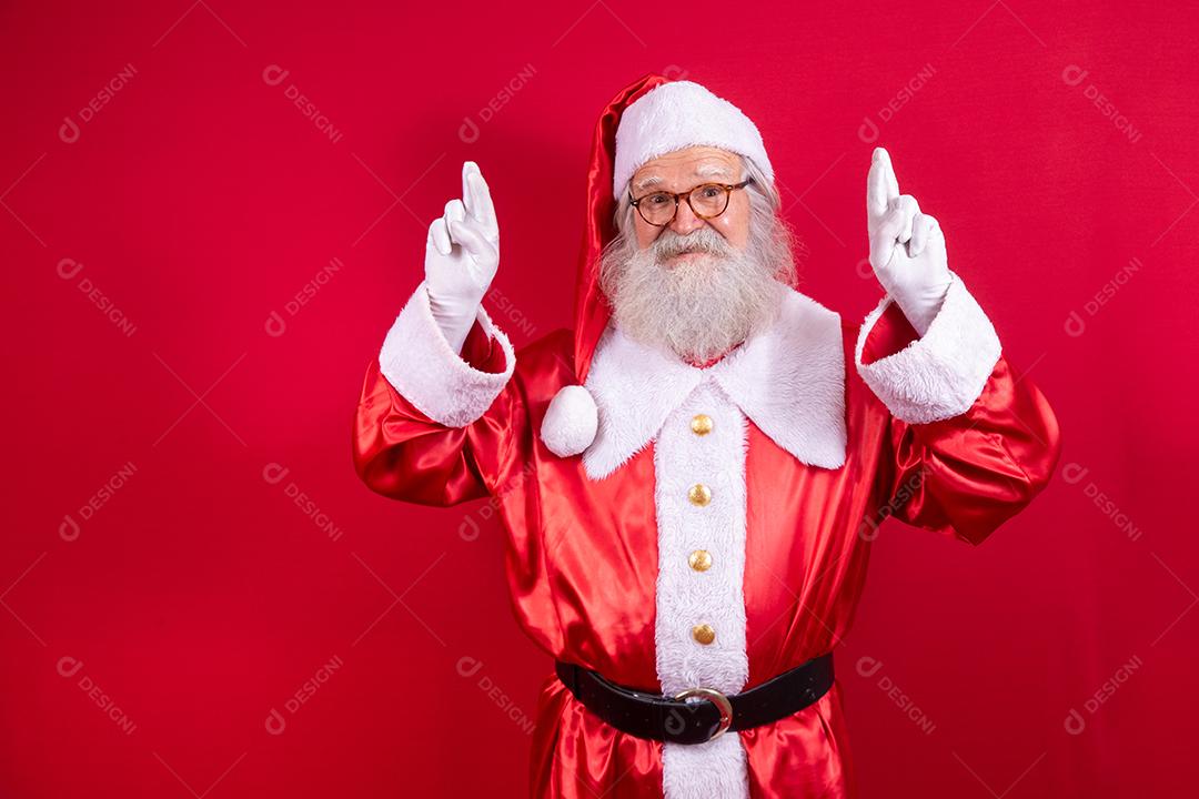 Retrato de um homem idoso sonhador em fantasia de papai noel cruzando os dedos fazendo um desejo