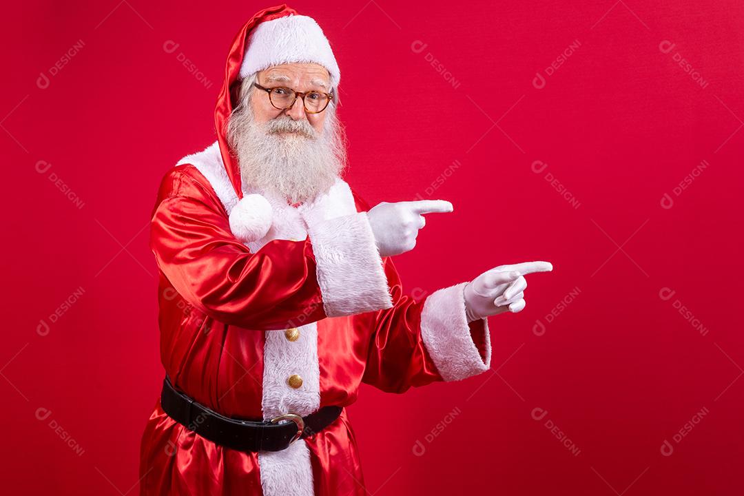 Engraçado feliz animado velho barbudo rosto de Papai Noel vestindo traje olhando para a câmera mostrando dedos apontando