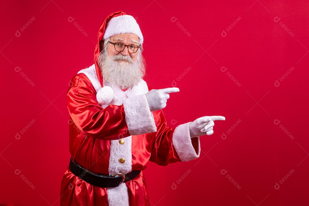 Engraçado feliz animado velho barbudo rosto de Papai Noel vestindo traje olhando para a câmera mostrando dedos apontando