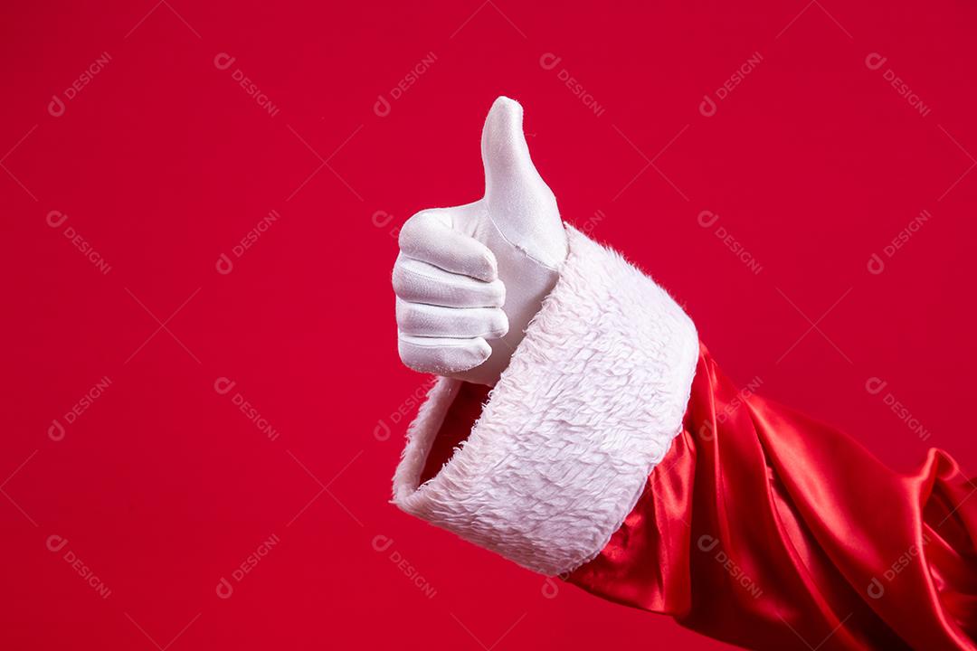 Mão enluvada do Papai Noel com o polegar para cima fazendo sinal okey sobre fundo vermelho. Feliz Ano Novo festivo