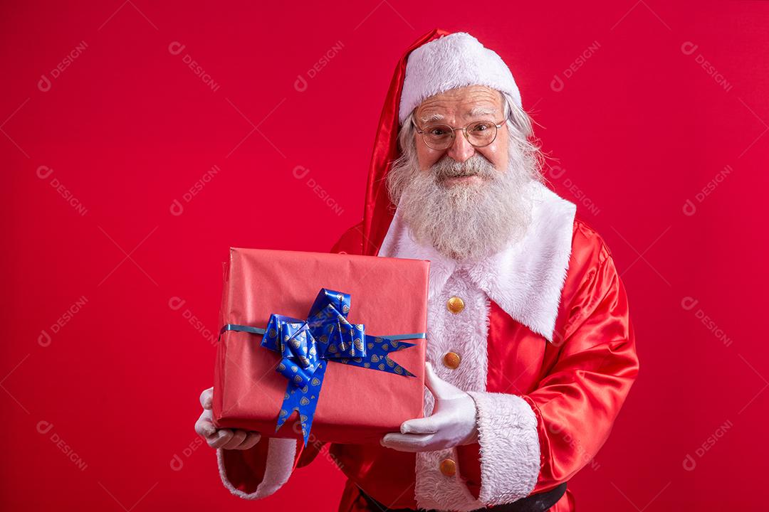 Papai Noel segurando um presente de Natal em fundo vermelho.