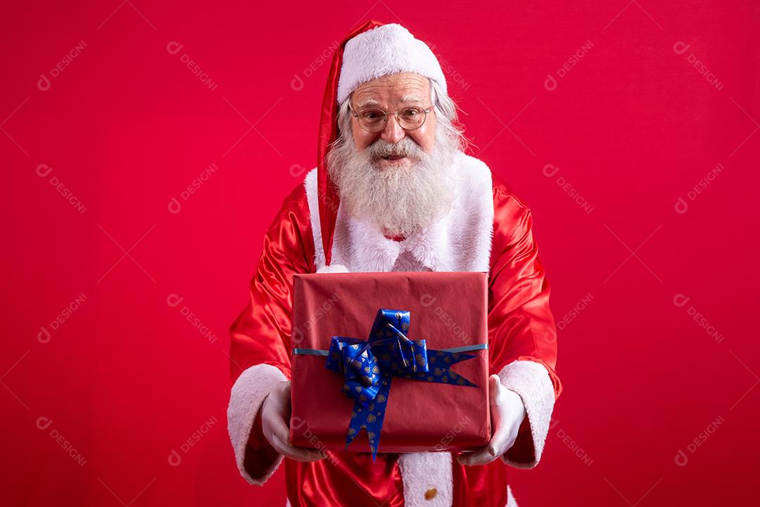 Papai Noel segurando um presente de Natal em fundo vermelho.