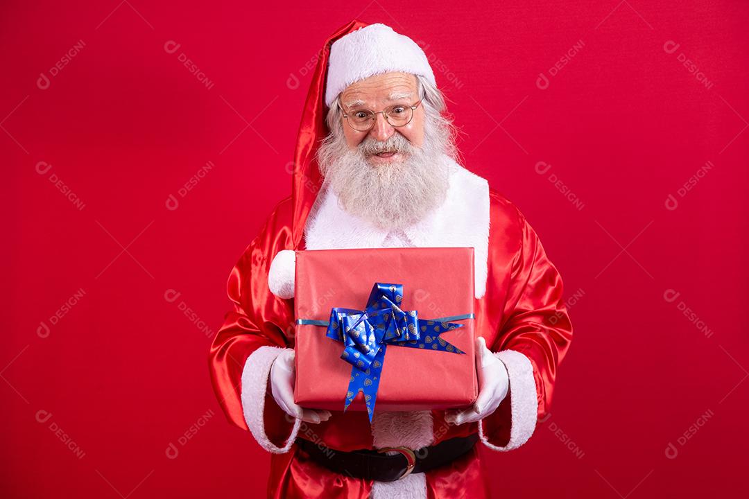 Papai Noel segurando um presente de Natal em fundo vermelho.