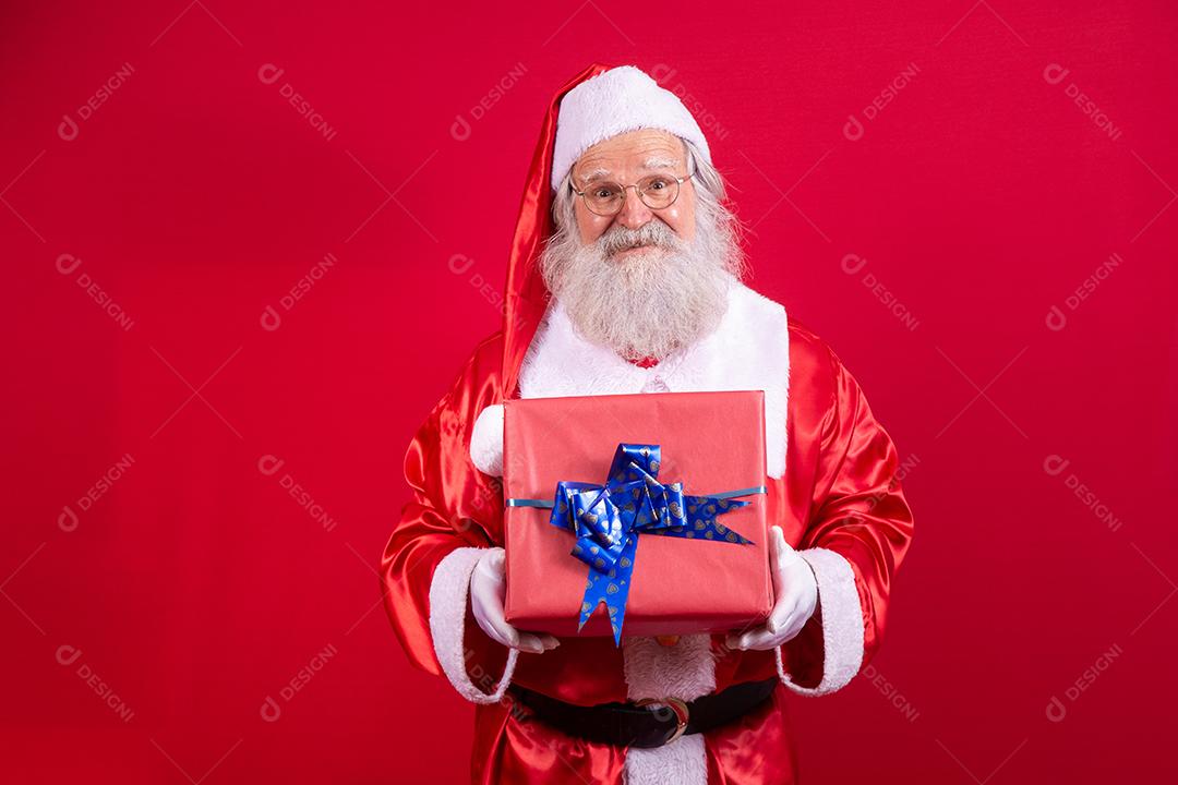 Papai Noel segurando um presente de Natal em fundo vermelho.