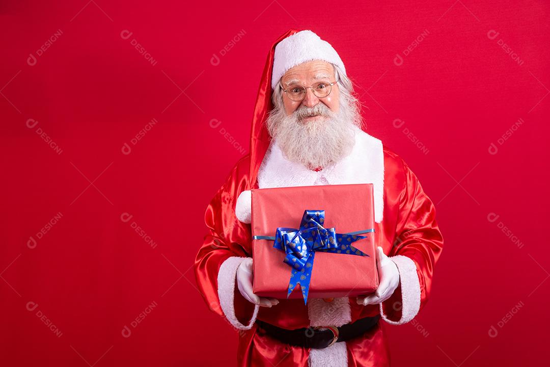 Papai Noel segurando um presente de Natal em fundo vermelho.
