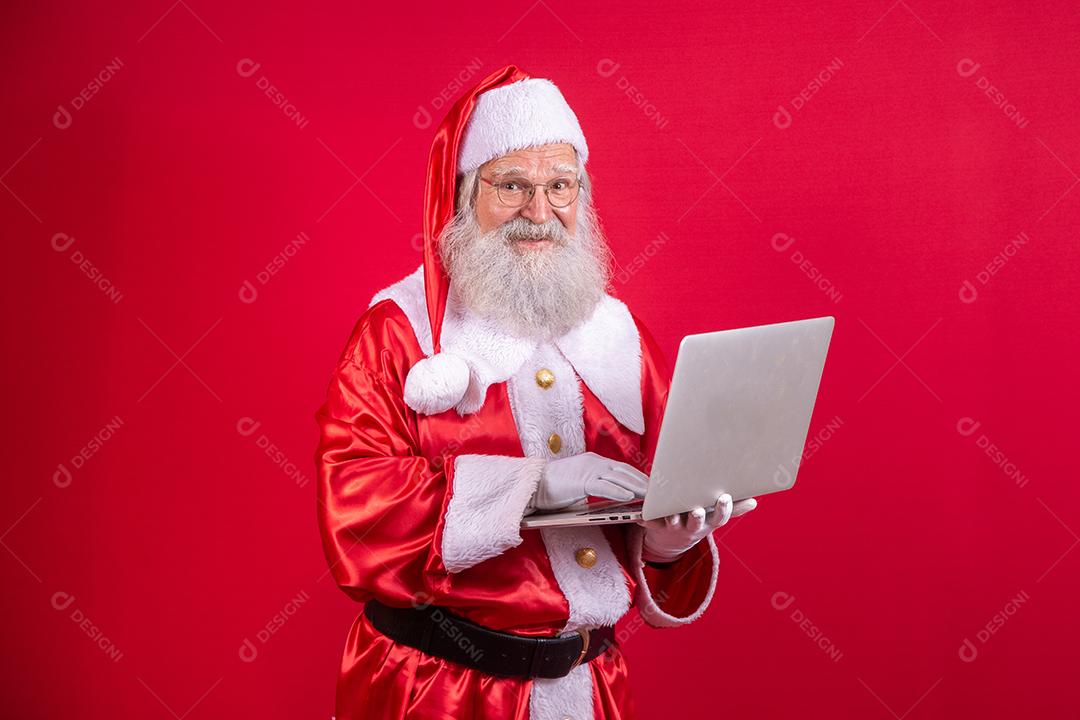 Papai Noel usando um laptop em fundo vermelho.