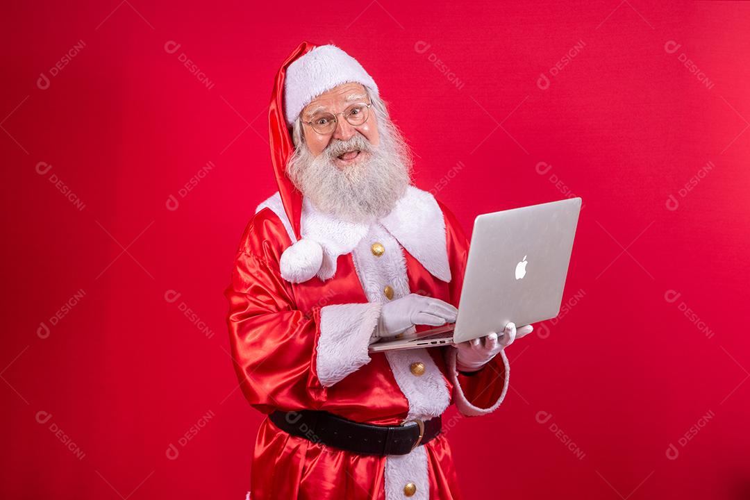 Papai Noel usando um laptop em fundo vermelho.