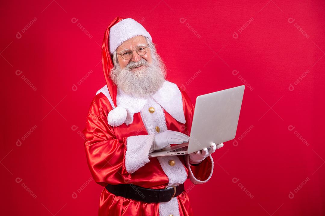 Papai Noel usando um laptop em fundo vermelho.