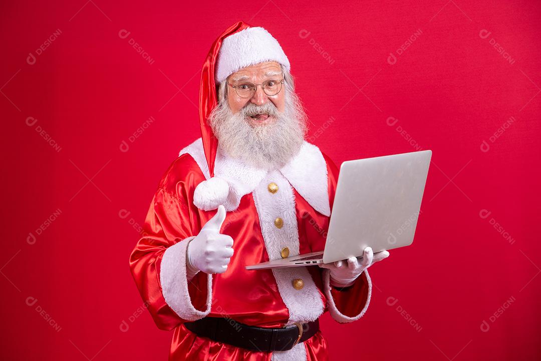 Papai Noel usando um laptop em fundo vermelho.