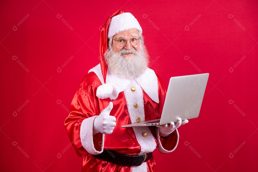 Papai Noel usando um laptop em fundo vermelho.