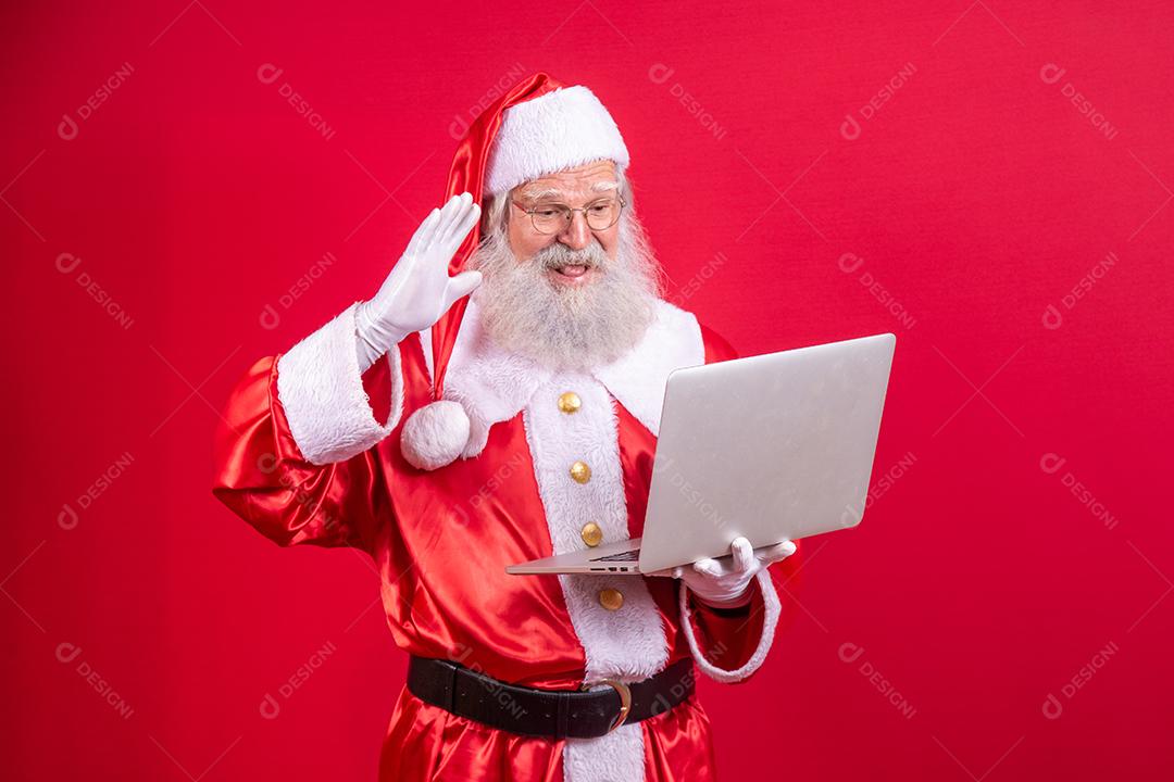 Papai Noel usando um laptop em fundo vermelho.