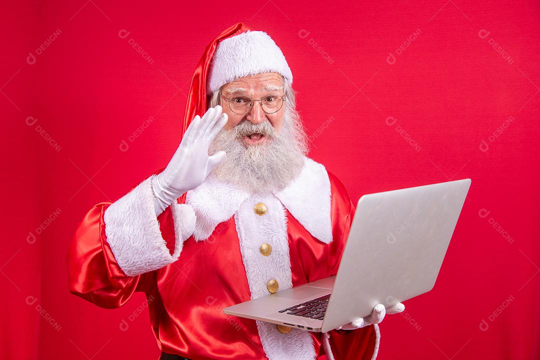 Papai Noel usando um laptop em fundo vermelho.