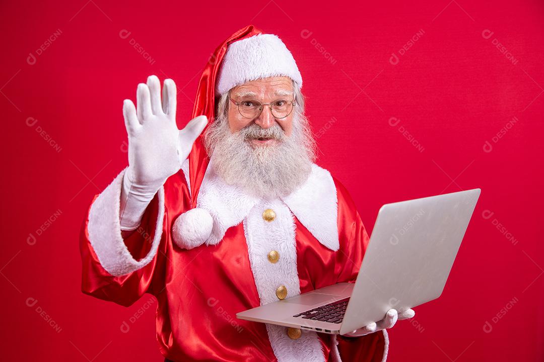 Papai Noel usando um laptop em fundo vermelho.