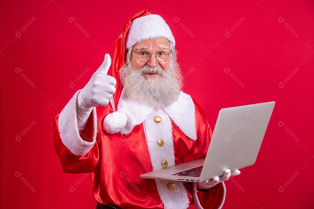 Papai Noel usando um laptop em fundo vermelho.