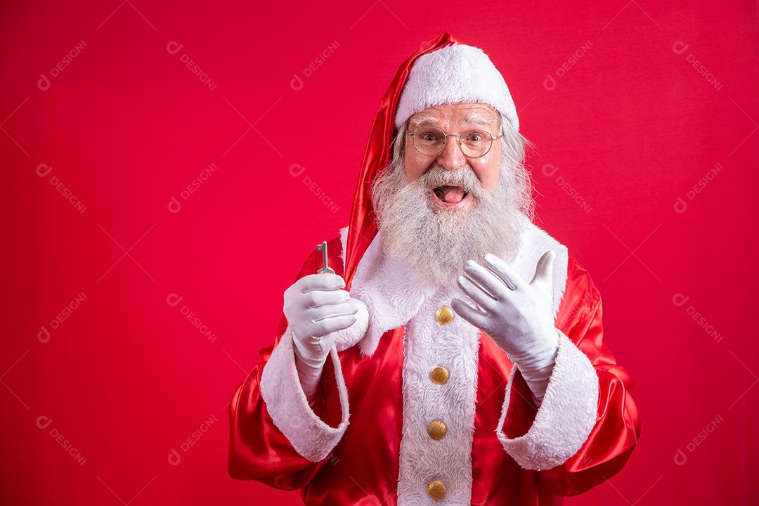 Papai Noel segurando as chaves da nova casa ou apartamento em fundo vermelho.