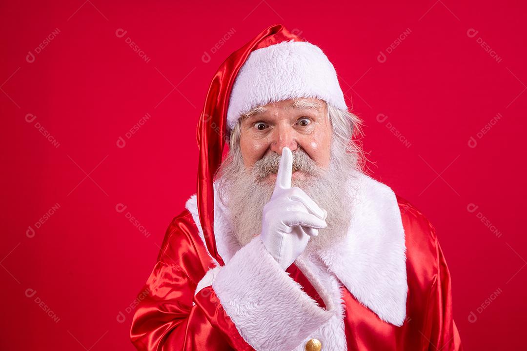 Papai Noel mantendo o dedo indicador pela boca e olhando para a câmera. Shh! Guarde segredo. Silencioso confidencial