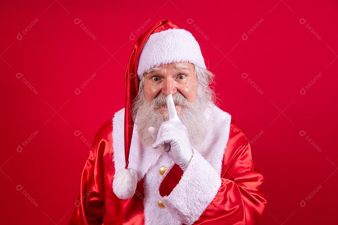Papai Noel mantendo o dedo indicador pela boca e olhando para a câmera. Shh! Guarde segredo. Silencioso confidencial