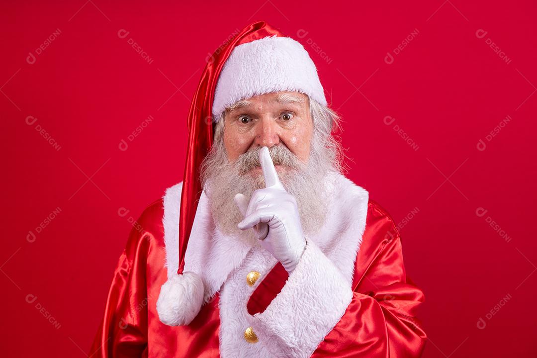 Papai Noel mantendo o dedo indicador pela boca e olhando para a câmera. Shh! Guarde segredo. Silencioso confidencial