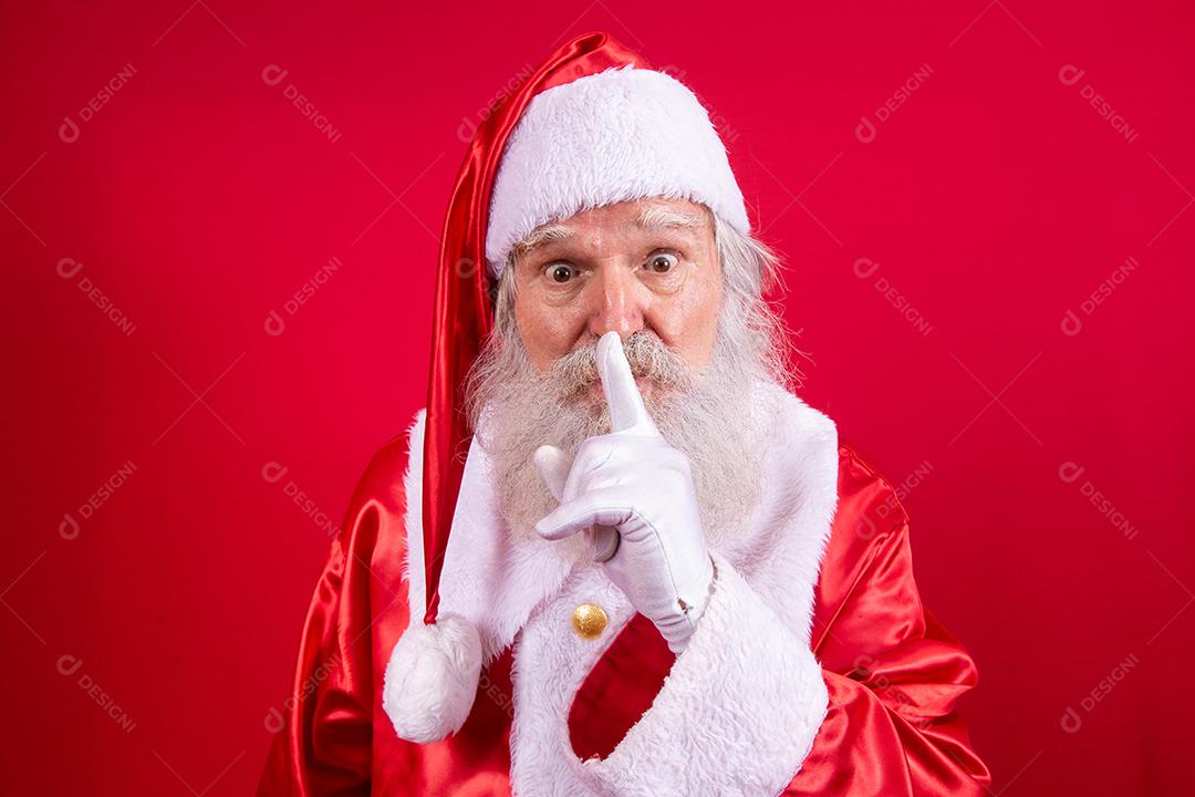 Papai Noel mantendo o dedo indicador pela boca e olhando para a câmera. Shh! Guarde segredo. Silencioso confidencial