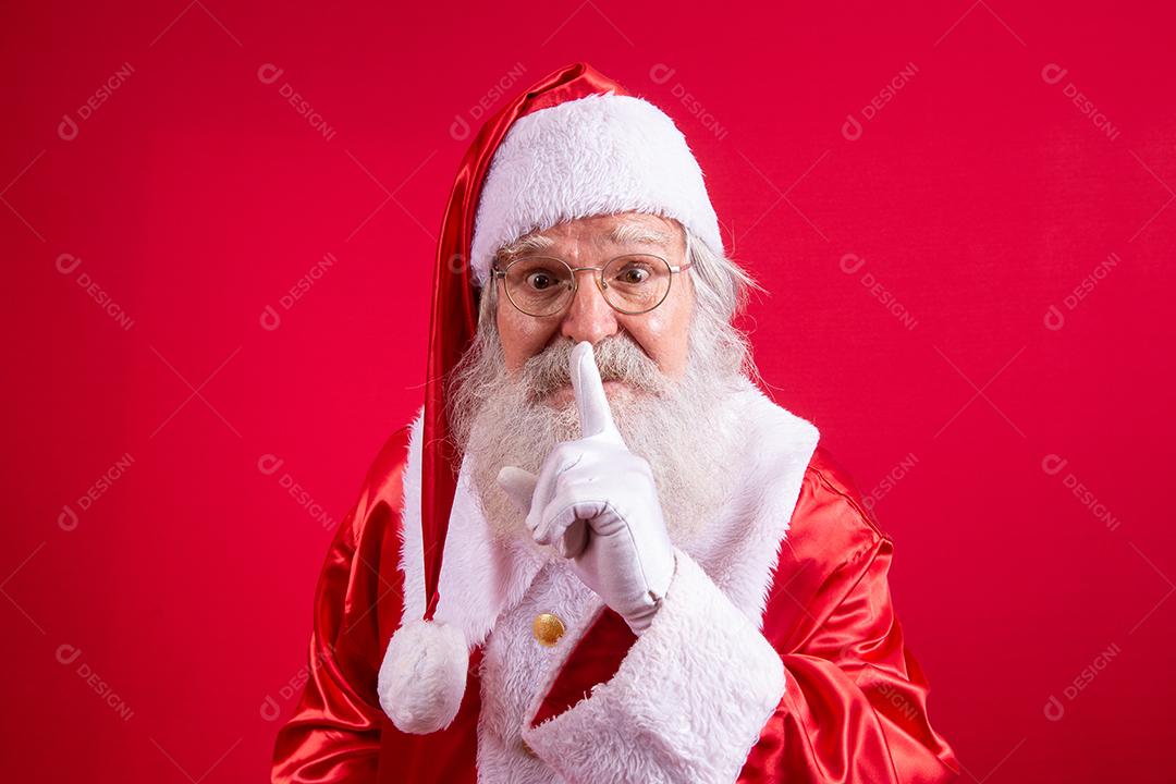 Papai Noel mantendo o dedo indicador pela boca e olhando para a câmera. Shh! Guarde segredo. Silencioso confidencial