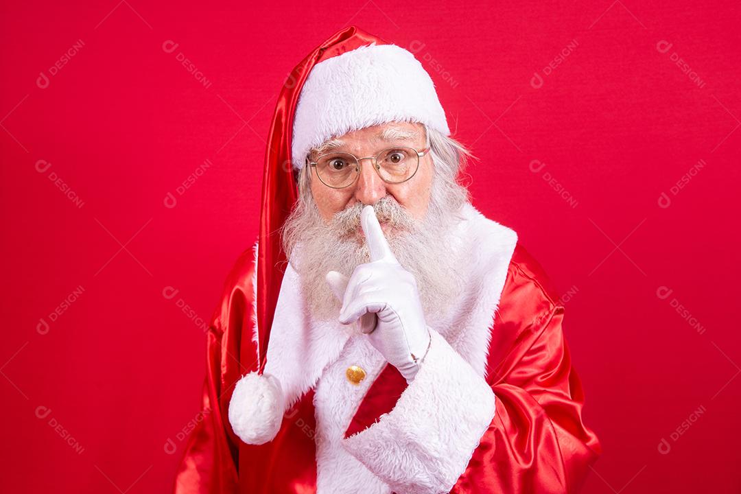 Papai Noel mantendo o dedo indicador pela boca e olhando para a câmera. Shh! Guarde segredo. Silencioso confidencial