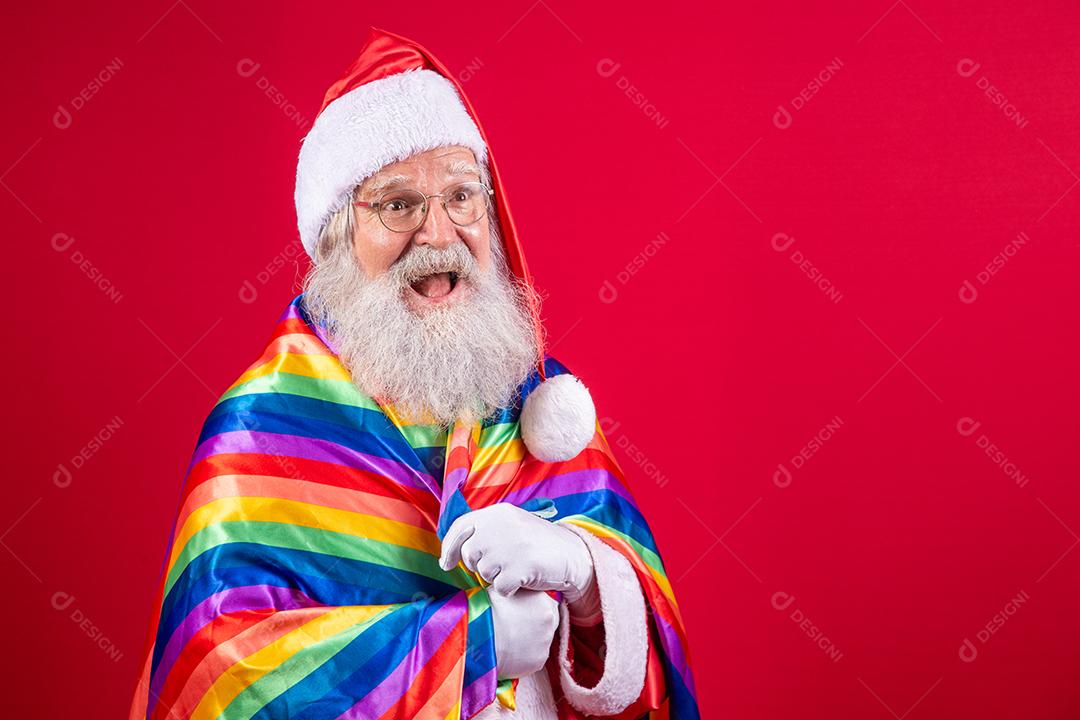 Papai Noel cobrindo com bandeira do orgulho LGBT. Sozinho. Um. Mantendo o punho erguido, cobrindo a bandeira LGBT. Bandeira LGBT + em fundo vermelho. Natal.